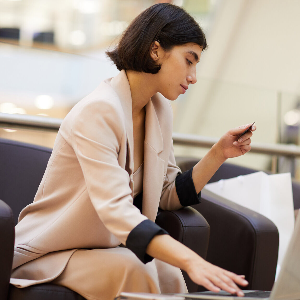 Portrait of elegant young woman holding credit card while using laptop enjoying e-shopping in mall, copy space